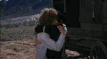 a man and a woman hugging in front of a wagon in the desert