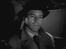 a man wearing a hat and a trench coat looks at the camera