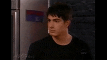 a young man in a black shirt is standing in front of a refrigerator with a sign on it that says abc fans