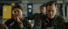 a man and a woman are sitting in a classroom and the man has a patch on his jacket that says " bob "