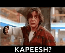 a man in a plaid shirt is pointing his fist at the camera with the words kapeesh ? below him .