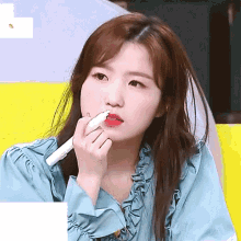a woman in a blue ruffled shirt is applying lipstick to her lips