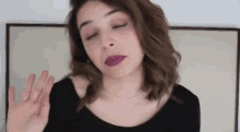 a woman wearing purple lipstick and a black shirt is making a funny face and waving her hand .