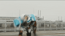 a person in a robotic suit is standing on a rooftop with a fence in the background