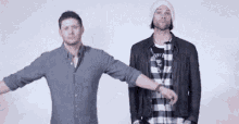 two men are standing next to each other with their arms outstretched in front of a white wall .