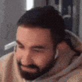 a man with a beard wearing headphones and a hoodie is sitting in front of a computer screen .