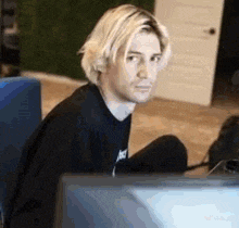 a man with blonde hair is sitting on the floor in front of a computer monitor .