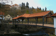 a bridge with a red tile roof over a river with a castle in the background