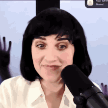 a woman wearing a black wig stands in front of a microphone with a screen behind her that says from teff pi thanks