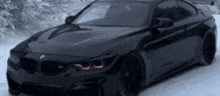 a black bmw m4 is driving in the snow .