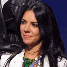a woman with long black hair and a white jacket smiles for the camera