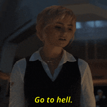 a woman in a white shirt and black vest says " go to hell "