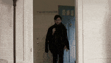 a man in a black coat and scarf is standing in a doorway