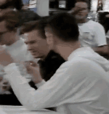a man in a white shirt sits at a table in a crowd