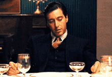 a man in a suit and tie is sitting at a table with glasses of wine