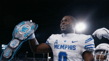 a football player wearing a memphis jersey holds a championship belt