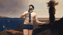 a shirtless man in a tie stands on a beach