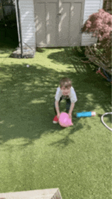 a young boy is playing with a pink balloon in a backyard