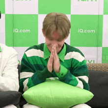 a man in a green and white striped shirt is sitting on a green pillow in front of a wall that says iq.com