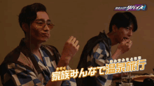 two men are sitting at a table with chinese writing on the bottom