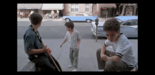 three young boys are playing on the sidewalk in front of a parking meter .