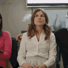 a woman in a white shirt is sitting in a waiting room with other people and looking up .