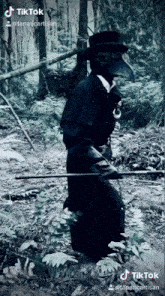 a man in a plague doctor costume is standing in the woods holding a stick