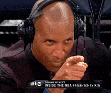 a man wearing headphones and a microphone is pointing at the camera with a nba advertisement behind him