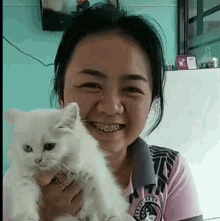 a woman is holding a white cat in her arms and smiling at the camera .