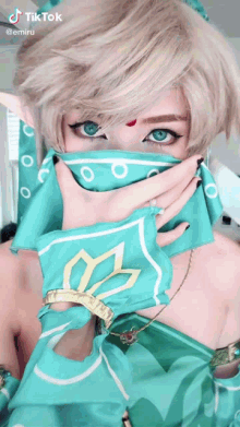 a woman with blonde hair and blue eyes is covering her face with a blue scarf .