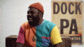 a man in a colorful shirt laughs in front of a sign that says dock pa