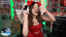 a woman wearing a red dress and a bunny headband is sitting in front of a sign that says feliz san valentin