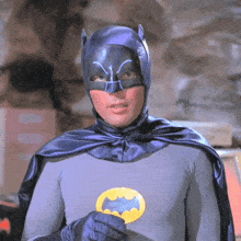 a man in a batman costume is holding a yellow bat emblem