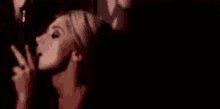 a woman is smoking a cigarette in a dark room and giving a peace sign .