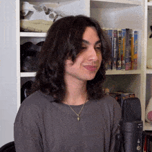 a woman stands in front of a microphone with a bookshelf behind her that has a book titled wizard of oz