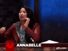a woman is sitting in front of a microphone with the name annabelle on the screen behind her .