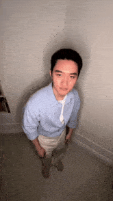 a man in a light blue shirt and khaki pants stands in a dark room