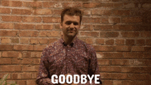 a man stands in front of a brick wall and says " goodbye "