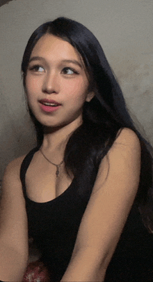 a woman with long black hair is wearing a black tank top and necklace