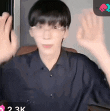 a young man wearing glasses and a blue shirt is waving his hands in the air .