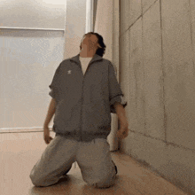 a man wearing a grey adidas jacket is kneeling on the floor