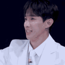 a man in a white suit and tie with a microphone on his neck is smiling .