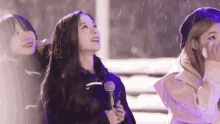 a group of young women are standing next to each other in the snow holding microphones .