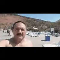 a shirtless man with a mustache is taking a selfie on the beach