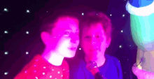 two young boys are standing next to each other in a dark room with glow in the dark lights behind them .