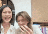 two women are laughing together in a room with books on the wall