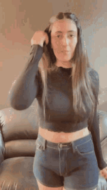 a woman wearing a black crop top and shorts is standing in front of a couch .