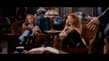 two women are sitting on a couch in a room with a lamp