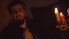 a man with a beard is standing in front of candles in a dark room