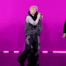 a man in a gray vest and black pants is dancing in front of a purple background .